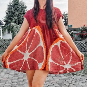 Puede incluir: Vestido corto de manga corta, de color rojo anaranjado. El vestido presenta un diseño de ganchillo de una rodaja de pomelo en la falda. La parte superior del vestido es de color rojo anaranjado liso.