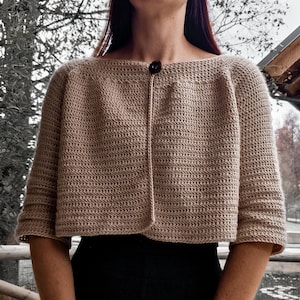 May include: A beige crocheted cardigan with a single button closure. The cardigan has a cropped length and three-quarter sleeves.