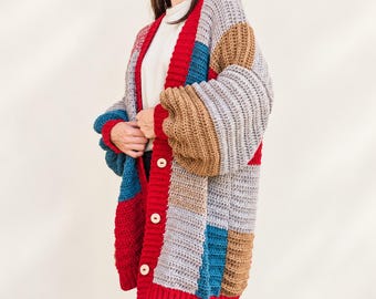 May include: A chunky crochet cardigan featuring a color-blocked pattern in shades of red, blue, tan, and grey. The garment has long sleeves, a ribbed red button placket with three light-colored circular buttons, and a ribbed red hem and cuffs.