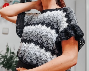 Pode incluir: Um top de crochê preto e branco com um padrão em ziguezague. O top tem mangas curtas com babados e um caimento solto.