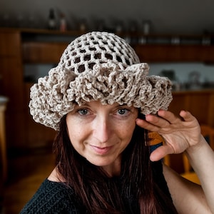 May include: A woman wearing a crocheted beige sun hat with a wide brim and a lacy design. The hat is made of a lightweight material and has a comfortable fit.