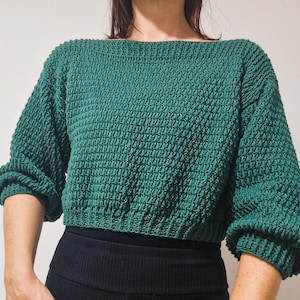 May include: A green knitted jumper with a boat neck and long sleeves. The jumper is cropped and has a textured knit.