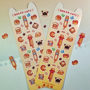 Puede incluir: Dos hojas de pegatinas con una variedad de gatos lindos vestidos como pan. Las pegatinas están sobre un fondo amarillo con el texto "Bread Cats" en la parte superior de cada hoja. Las pegatinas son perfectas para agregar un toque de fantasía a tu agenda, computadora portátil o botella de agua.
