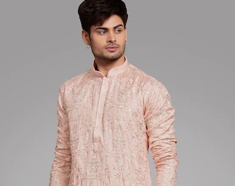 May include: A peach-coloured long-sleeved kurta with white embroidery. The kurta has a mandarin collar and a button closure. The model is wearing white trousers and black shoes.