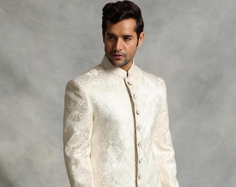 May include: A cream-coloured jacket with a mandarin collar and button closure. The jacket has a subtle geometric pattern. The person is wearing the jacket in front of a grey background.