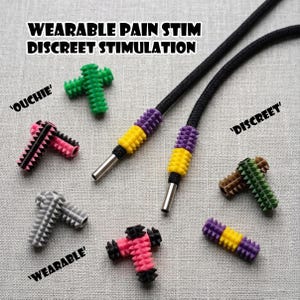 May include: A selection of wearable pain stim devices in green, pink, grey, and brown. The image also shows black cords with purple and yellow details, and the text "WEARABLE PAIN STIM DISCREET STIMULATION".