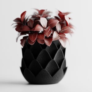 Könnte beinhalten: Eine schwarze, strukturierte Vase mit einem einzigartigen, geschichteten Design, gefüllt mit weinroten Blättern. Die Vase hat einen abgerundeten Boden und eine strukturierte Oberfläche, die einen auffälligen Kontrast zum zarten Laub der Pflanze bildet.