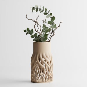 May include: A beige ceramic vase with a root-like pattern on the lower section. It contains green eucalyptus leaves and slender, brown branches. The vase is a decorative home decor item.