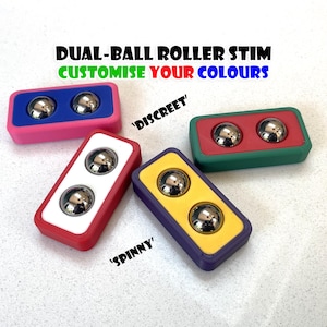 Può includere: Diversi giocattoli stimolanti a rullo a doppia sfera in vari colori. Ogni giocattolo rettangolare ha due sfere di metallo argentato. I giocattoli sono rosa, blu, rosso, bianco, giallo, verde e viola. Il testo sull'immagine recita "DUAL-BALL ROLLER STIM PERSONALIZZA I TUOI COLORI".