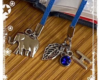 May include: Two blue ribbon bookmarks with silver charms. One charm is an elephant, the other has a leaf, a blue gemstone, and the letter H.