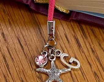 May include: Pink and silver bookmark with a charm of a starfish, a pink rhinestone, and a letter "G".