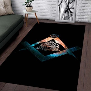 May include: A black rug with a white all-seeing eye design inside a triangle, surrounded by a compass and square. The design is set against a blue and orange galaxy background.