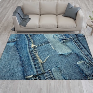 May include: A rectangular area rug with a denim patchwork design. The rug features various shades of blue denim, with visible stitching and distressed details. The rug is placed on a light-colored wooden floor, with a beige sofa and a small side table in the background.
