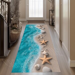 Peut inclure: Un tapis de couloir rectangulaire présentant une impression haute résolution d'un rivage sablonneux. Le motif affiche des vagues turquoise s'échouant sur du sable beige, décoré de coquillages blancs et de deux étoiles de mer orange.