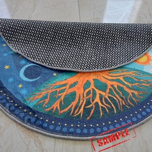 May include: A round, blue and orange rug with a tree of life design. The rug has a black and white patterned backing. The rug has the word "SAMPLE" written on it.