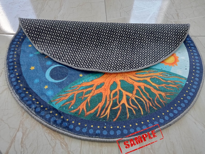 May include: A round, blue and orange rug with a tree of life design. The rug has a black and white patterned backing. The rug has the word "SAMPLE" written on it.