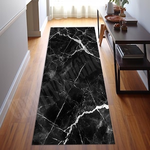Può includere: Un tappeto runner rettangolare nero con motivo marmorizzato e venature bianche. Il tappeto è posato su un pavimento in legno in un corridoio. Il design del tappeto ricorda la pietra naturale, aggiungendo un tocco di eleganza allo spazio.