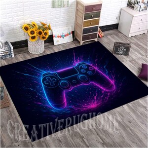 May include: A rectangular black rug featuring a neon blue and pink video game controller design. The controller is outlined with a glowing effect against a dark background. The rug has the text "CREATIVE RUGS HOME" at the bottom.