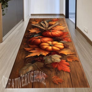 May include: A rectangular runner rug featuring a printed design of orange pumpkins, brown pinecones, and golden wheat stalks arranged on a dark brown wood grain background. The text CREATIVERUGHOME is printed in white near the bottom edge.