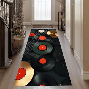 May include: A black and gold runner rug with a design of stacked vinyl records. The records have red and white labels.