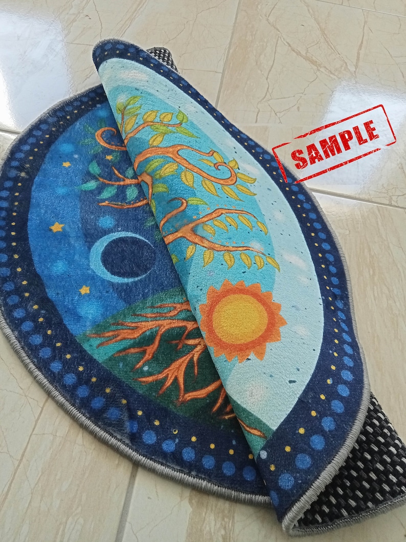 May include: A round, blue and yellow rug with a tree design and a sun and moon on either side. The rug has a gray border and a black non-slip backing.