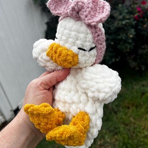 K&ouml;nnte beinhalten: Handgeh&auml;kelte Enten-Pl&uuml;schfigur mit wei&szlig;em K&ouml;rper, gelbem Schnabel und F&uuml;&szlig;en sowie einem rosa Schleifen-Stirnband. Das weiche, flauschige Spielzeug ist f&uuml;r Kinder geeignet.