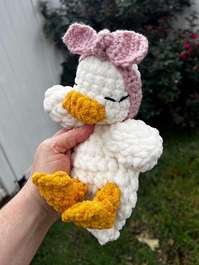 K&ouml;nnte beinhalten: Handgeh&auml;kelte Enten-Pl&uuml;schfigur mit wei&szlig;em K&ouml;rper, gelbem Schnabel und F&uuml;&szlig;en sowie einem rosa Schleifen-Stirnband. Das weiche, flauschige Spielzeug ist f&uuml;r Kinder geeignet.