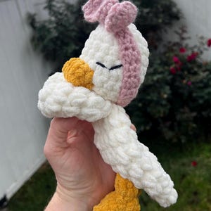 K&ouml;nnte beinhalten: Ein handgefertigtes H&auml;kelenten-Spielzeug in Wei&szlig;, Gelb und Rosa. Die Ente hat einen wei&szlig;en K&ouml;rper, einen gelben Schnabel und F&uuml;&szlig;e sowie ein rosa Stirnband. Das Spielzeug ist weich und flauschig, perfekt f&uuml;r das Spiel eines Kindes oder die Dekoration des Kinderzimmers.
