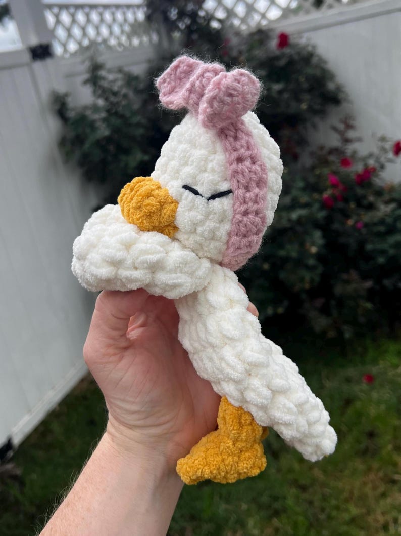 K&ouml;nnte beinhalten: Ein handgefertigtes H&auml;kelenten-Spielzeug in Wei&szlig;, Gelb und Rosa. Die Ente hat einen wei&szlig;en K&ouml;rper, einen gelben Schnabel und F&uuml;&szlig;e sowie ein rosa Stirnband. Das Spielzeug ist weich und flauschig, perfekt f&uuml;r das Spiel eines Kindes oder die Dekoration des Kinderzimmers.