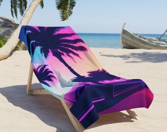 May include: A beach towel featuring a pink, blue and purple sunset scene with palm trees silhouetted against the sky. The towel is folded and placed on a wooden beach chair.