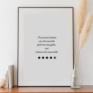 May include: A framed print with a black frame and a white background. The print features a quote about positive thinking: "The positive thinker sees the invisible, feels the intangible, and achieves the impossible." Five black stars are below the quote.