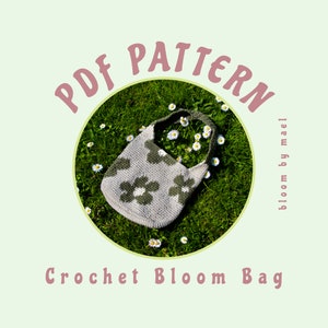 May include: PDF pattern for a crochet bag with a flower design. The bag is light gray with green flowers and is lying on a bed of green grass with white daisies. The text "PDF PATTERN" is in pink and the text "bloom by mael" is in gray. The text "Crochet Bloom Bag" is in pink.