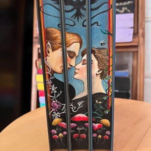 May include: Three hardcover books with custom painted edges. The edges feature a blue background with a painted illustration of two people, mushrooms, and a bee. The spines are blue.