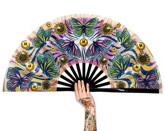 May include: A colorful hand fan with a black handle and a white background. The fan is decorated with butterflies, sunflowers, and smiley faces.