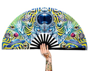 May include: A black and white folding fan with a colorful design of an astronaut in a psychedelic space scene. The astronaut is wearing a blue and white spacesuit and has a yellow background with blue and green swirls. The fan is open and held by a hand.