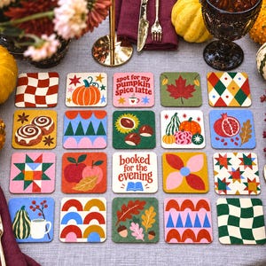 Könnte beinhalten: Ein Set aus zwanzig quadratischen Untersetzern mit verschiedenen herbstlichen Illustrationen, darunter Kürbisse, Blätter, Granatäpfel sowie die Texte "spot for my pumpkin spice latte" und "booked for the evening" auf einer grauen Tischdecke.