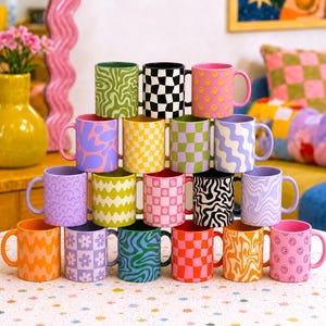 May include: A collection of seventeen ceramic mugs stacked in a pyramid formation. Each mug features a distinct pattern, including checkerboard, wavy lines, floral motifs, and smiley faces, rendered in a variety of bright and pastel colors.