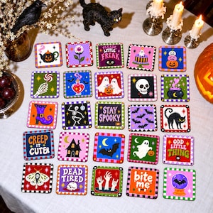 Könnte beinhalten: Eine Sammlung von fünfundzwanzig quadratischen Untersetzern mit farbenfrohen Halloween-Illustrationen, darunter Geister, Skelette, Kürbisse, Fledermäuse und Texte wie 'PLEASE LITTLE FREAK', 'STAY SPOOKY', 'CREEP IT CUTE', 'DEAD TIRED', 'ODD LITTLE THING' und 'bite me'.