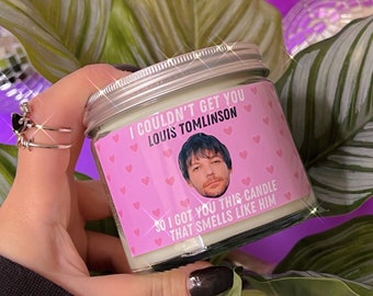Könnte beinhalten: Eine rosa Kerze mit einem Etikett, auf dem steht: "Ich konnte dich nicht bekommen, Louis Tomlinson, also habe ich dir diese Kerze besorgt, die nach ihm riecht." Das Etikett zeigt auch ein Foto von Louis Tomlinson und rosa Herzen.