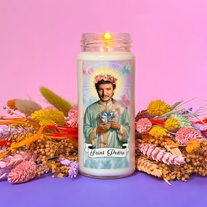 Peut inclure: Une bougie blanche avec une image d'un homme portant une couronne de fleurs et tenant un cœur bleu. La bougie porte l'inscription "Saint Pedro" en bas.