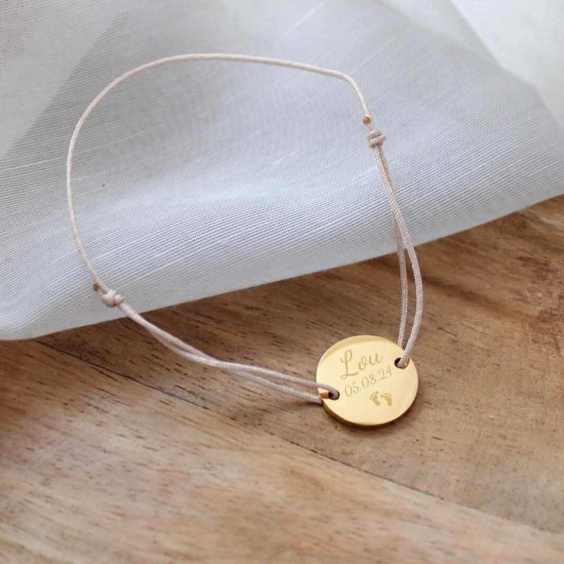 May include: A gold bracelet with a round charm that says "Lou 05.08.24" with a pair of footprints.