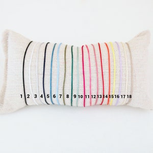 May include: A close-up of 18 different colored cords, numbered 1 through 18, displayed on a white pillow. The cords are all the same thickness and are arranged in a row.