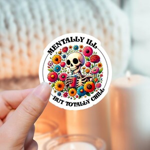 Könnte beinhalten: Ein runder Aufkleber mit einem farbenfrohen Blumendesign und einem Skelett, das ein Getränk hält. Der Text lautet "Mentally Ill But Totally Chill".