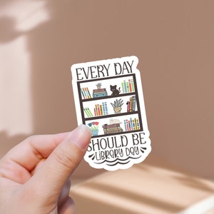 Könnte beinhalten: Ein weißer Aufkleber mit einer schwarzen Bücherregal-Illustration und dem Text "Every day should be library day".