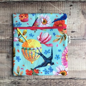 May include: A rectangular fabric pouch with a light blue background featuring a colorful print of hot air balloons, swallows, and various flowers. The pouch has a bright pink horizontal zipper closure with a yellow pull tab and a small white tag.