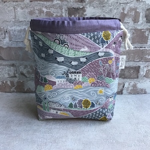 May include: A purple drawstring bag with a countryside scene printed on it. The scene features a house, trees, sheep, a tractor, and a river. The bag has a white drawstring and a label that says "Hope Grey".