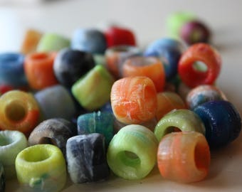 May include: A collection of colorful, cylindrical beads in various shades of orange, blue, green, and red. The beads have a hole through the center and appear to be made of a translucent material.