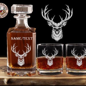 May include: A set of two clear glass whiskey glasses and a clear glass decanter with a deer head design etched on each. The decanter has the text "NAME/TEXT" on the front.