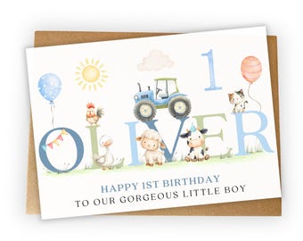 May include: A greeting card with a brown envelope. The card features a watercolor illustration of a blue tractor, farm animals, a sun, and a balloon. The text reads "OLIVER" and "HAPPY 1ST BIRTHDAY TO OUR GORGEOUS LITTLE BOY."