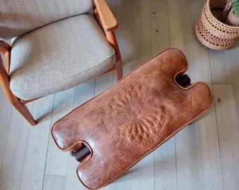 アンティークのラクダの鞍、素朴な木製の足置き、古びた素朴な布張りの